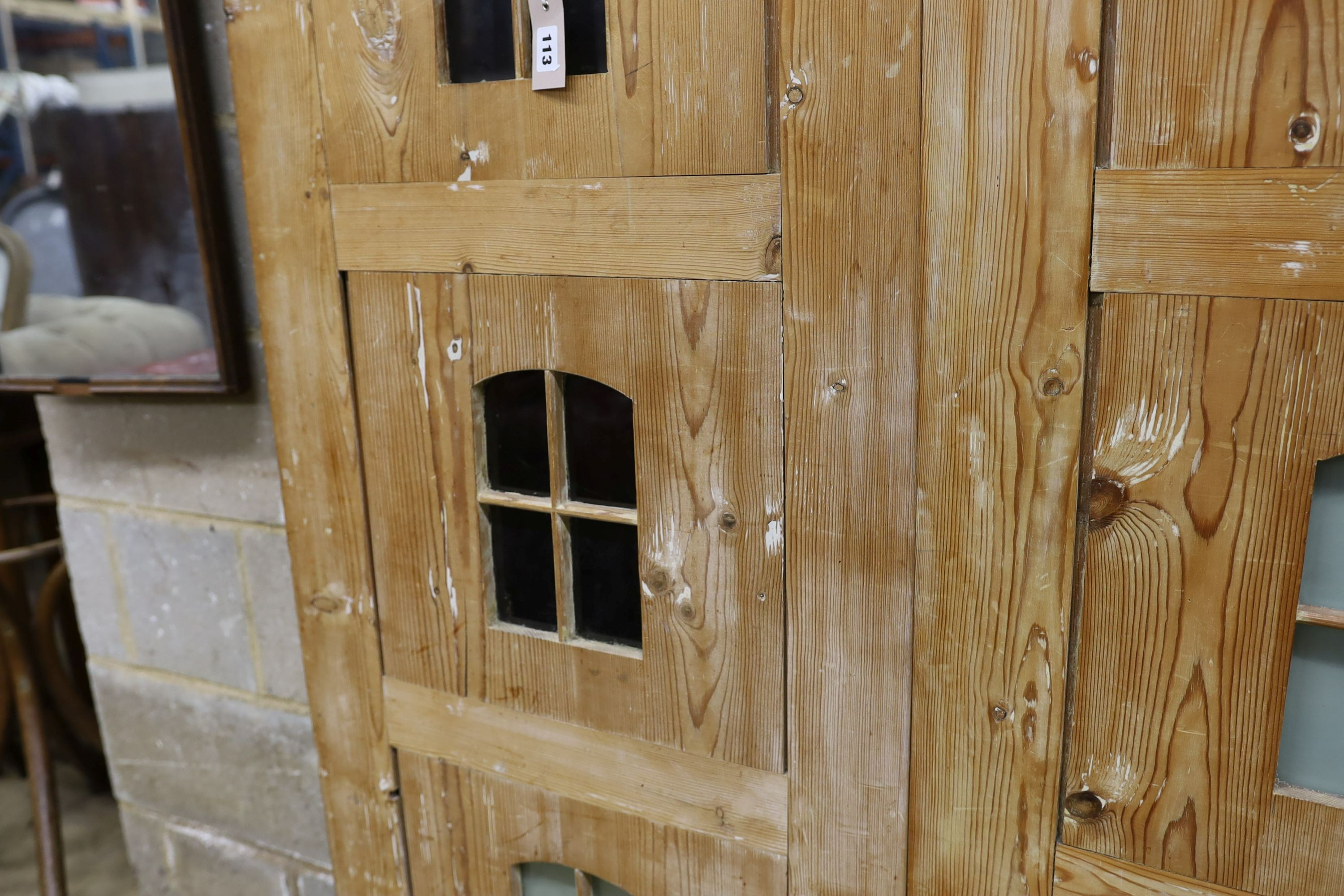 A 19th century stripped pine hall cupboard modelled as a dolls house the two door nine window facade enclosing a compartmented interior, width 182cm, depth 46cm, height 192cm